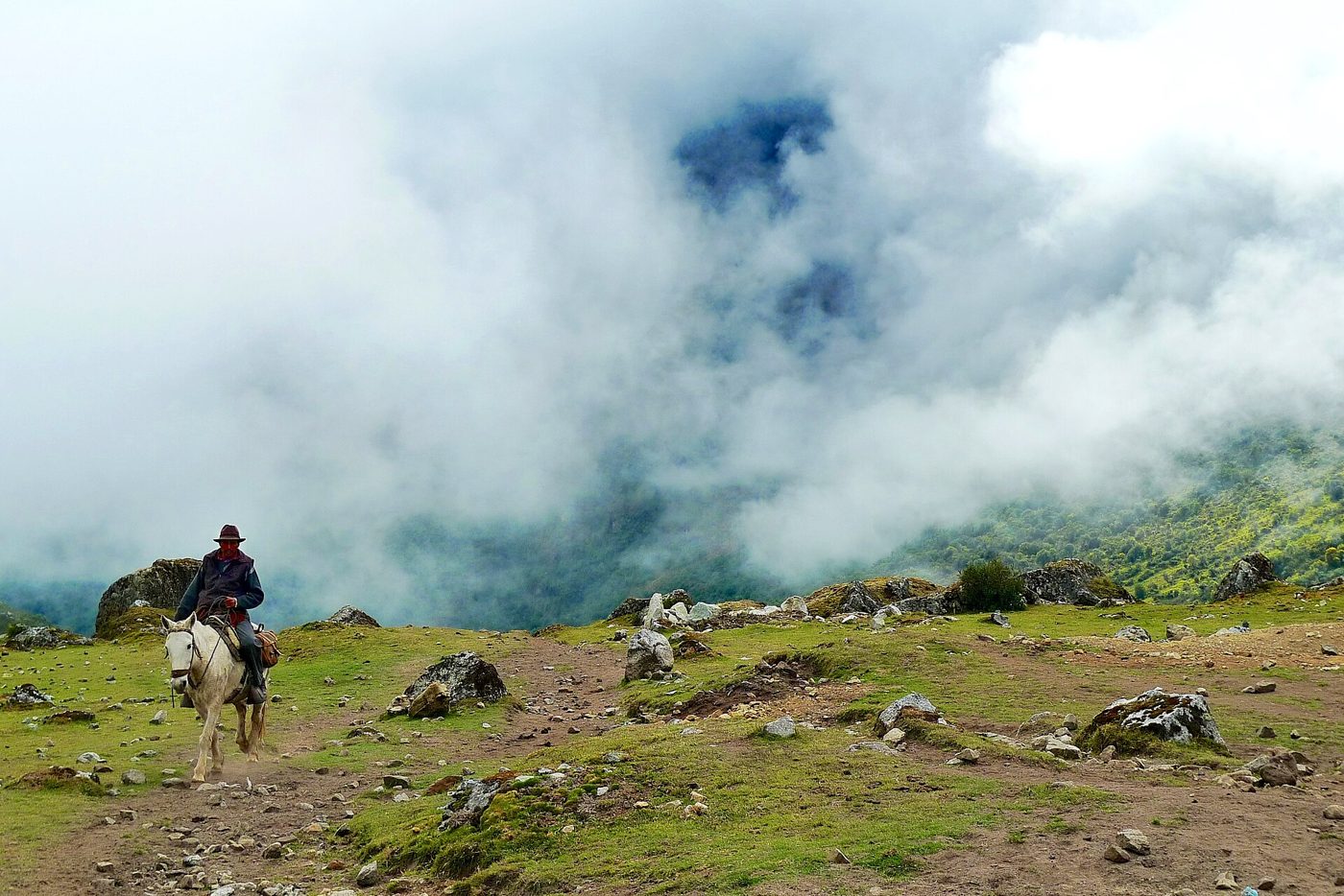 A rider on a mountain trail under rolling cloud.